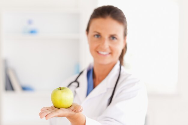 Доктор со стетоскопом, держащий яблоко, глядя на камеру