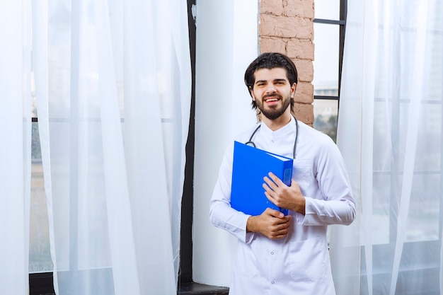 Doctor with a stethoscope holding a blue reporting folder. 