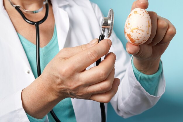 Doctor with stethoscope holding Easter pink egg on blue