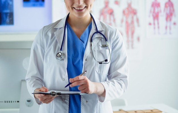 Doctor with a stethoscope, holding a notebook in his hand. Close-up of a female doctor filling up medical form at clipboard while standing straight in hospital