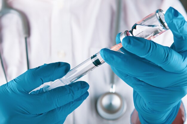 Doctor with stethoscope on the neck and wearing medical glove holding syringe and vial of the vaccine