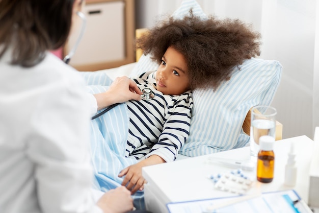 ステトスコープを持った医者とベッドに横たわっている病気の女の子
