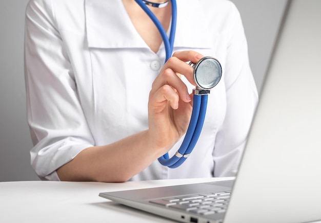 Doctor with stethoscope speaking to patient through video chat Woman in lab coat advising client with illness injury using laptop Online medicine consultation and diagnostics concept