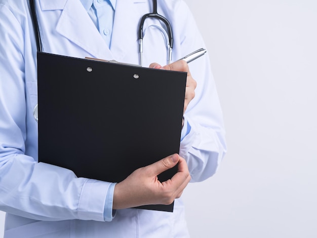 Doctor with stethoscope in white coat holding clipboard writing medical record diagnosis isolated on white background close up cropped view