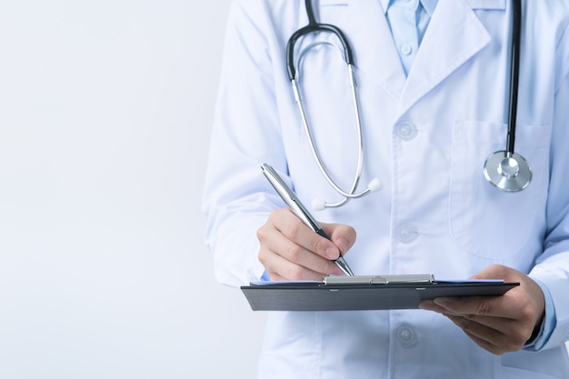 Doctor with stethoscope in white coat holding clipboard, writing medical record diagnosis, isolated on white background, close up, cropped view.