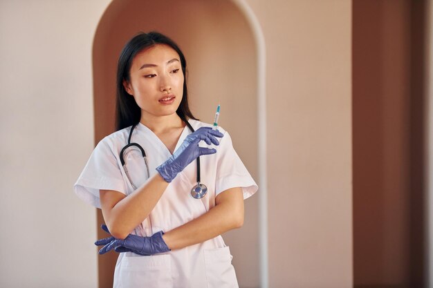 Doctor with syringe Young serious asian woman standing indoors