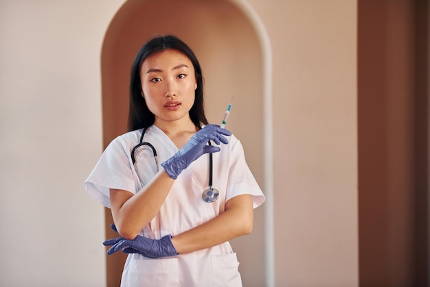 Doctor with syringe Young serious asian woman standing indoors