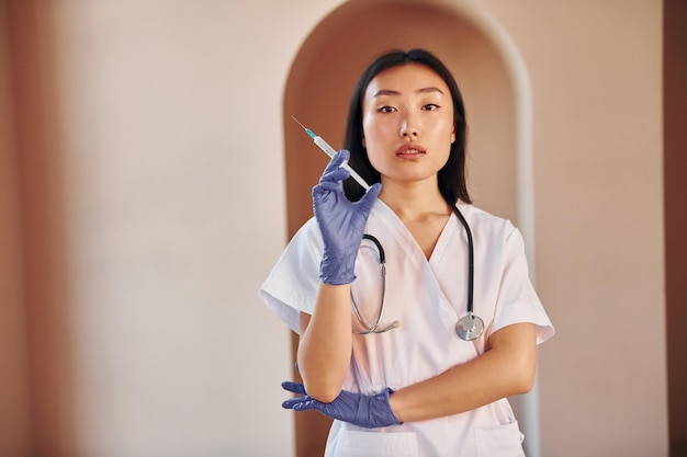 Doctor with syringe Young serious asian woman standing indoors