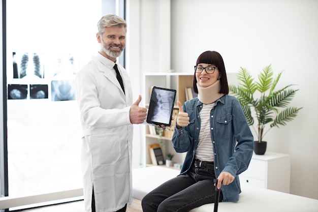 Doctor with tablet and lady in neck brace posing in clinic