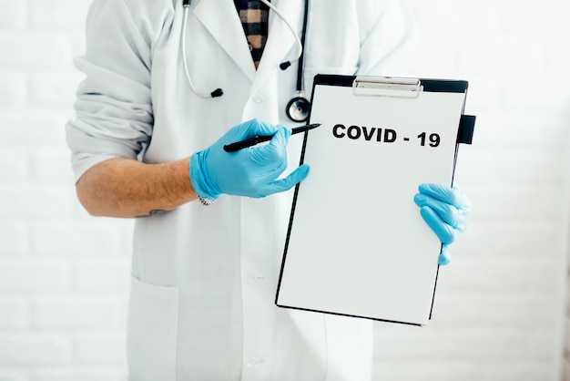 흰색 배경에 태블릿이 있는 의사는 펜 covid-19로 질병의 이름을 보여줍니다