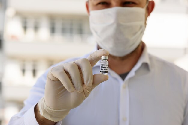白い手袋をした医師は、COVID-19ワクチンのボトルを保持します