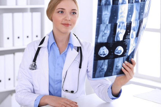 Doctor woman examining x-ray picture near window in hospital. Surgeon or orthopedist at work. Medicine and healthcare concept. Blue colored blouse of a therapist looks good.