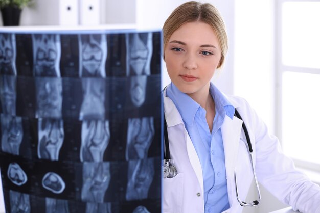 Женщина-врач изучает рентгеновский снимок возле окна в больнице. Хирург или ортопед на работе. Концепция медицины и здравоохранения. Хорошо смотрится голубая блузка терапевта.