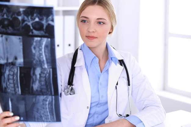 Doctor woman examining x-ray picture near window in hospital. Surgeon or orthopedist at work. Medicine and healthcare concept. Blue colored blouse of a therapist looks good.