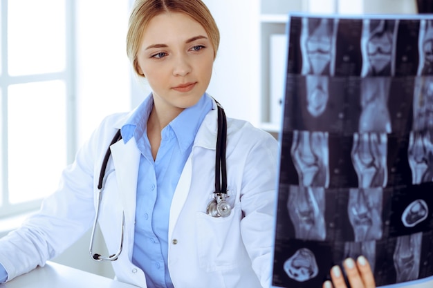 Doctor woman examining x-ray picture near window in hospital. Surgeon or orthopedist at work. Medicine and healthcare concept. Blue colored blouse of a therapist looks good.