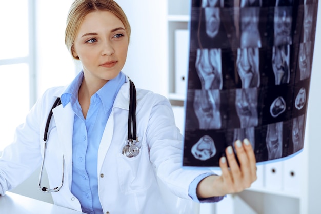 병원 창 근처에서 엑스레이 사진을 검사하는 의사 여자. 직장에서 외과 의사 또는 정형 외과 의사. 의학 및 의료 개념입니다. 치료사의 파란색 블라우스가 잘 어울립니다.
