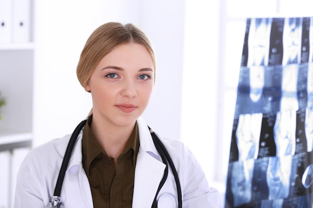 Doctor woman examining x-ray picture near window in hospital. Surgeon or orthopedist at work. Medicine and healthcare concept. Khaki colored blouse of a therapist looks good.