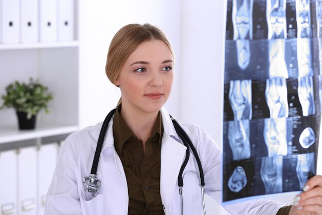 Doctor woman examining x-ray picture near window in hospital. Surgeon or orthopedist at work. Medicine and healthcare concept. Khaki colored blouse of a therapist looks good.