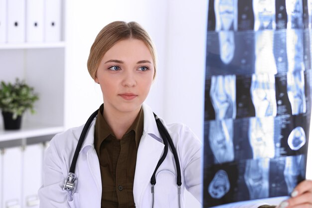 Doctor woman examining x-ray picture near window in hospital. Surgeon or orthopedist at work. Medicine and healthcare concept. Khaki colored blouse of a therapist looks good.