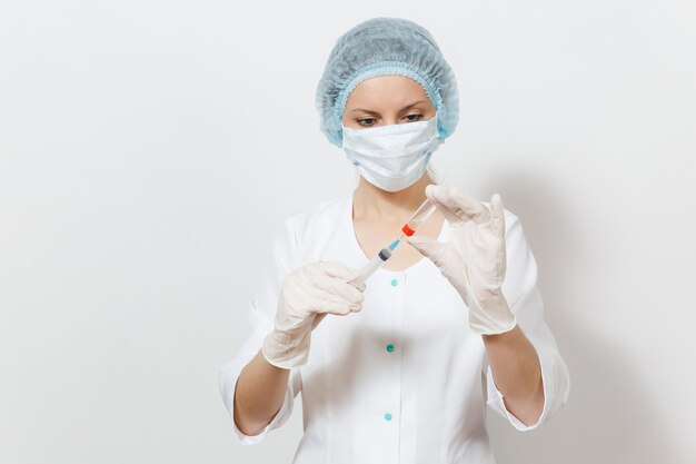 Doctor woman in face mask, sterile hat, gloves draws liquid medicine from bottle with syringe with needle isolated on white background. Female doctor in medical gown. Healthcare personnel concept.