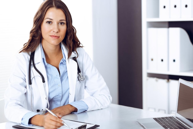 Doctor woman filling up medical form while sitting at the desk in hospital office. Physician at work. Medicine and health care concept.