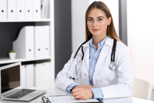 Doctor woman filling up medical form while sitting at the desk in hospital office. Physician at work. Medicine and health care concept.