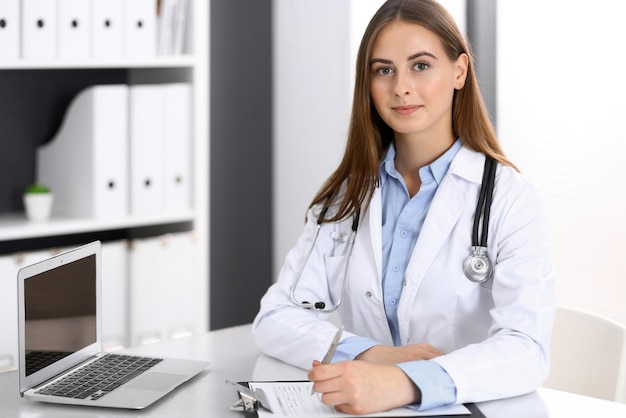 Doctor woman filling up medical form while sitting at the desk in hospital office. Physician at work. Medicine and health care concept.