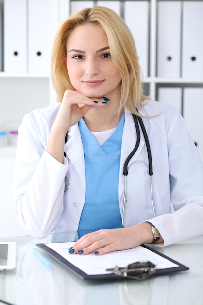 책상에 앉아있는 동안 의료 양식을 작성하는 의사 여자. 의학 및 건강 관리 개념입니다.
