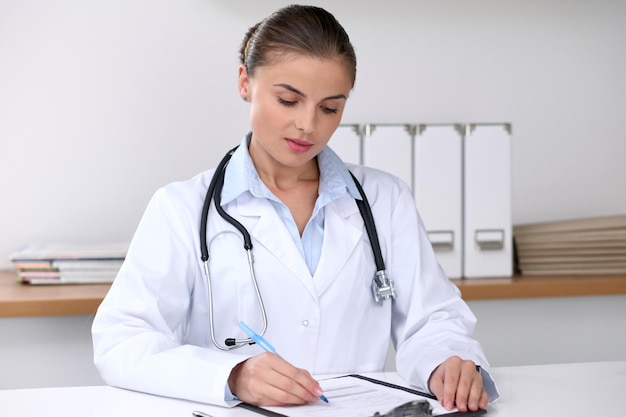 Doctor woman filling up medical form while sitting at the desk Medicine and health care concept