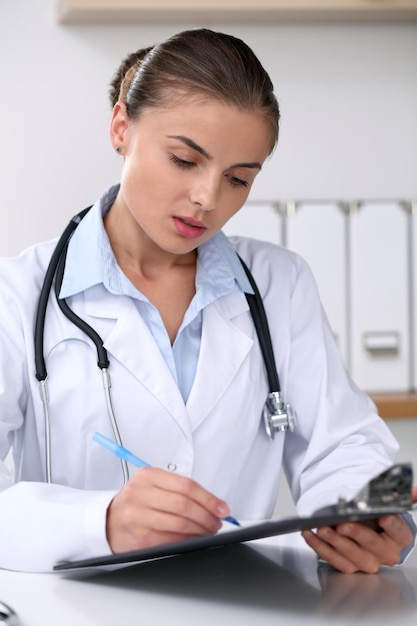 Doctor woman filling up medical form while  sitting at the desk. Medicine and health care concept