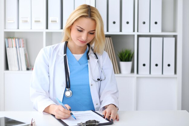 Doctor woman filling up medical form while  sitting at the desk. Medicine and health care concept.