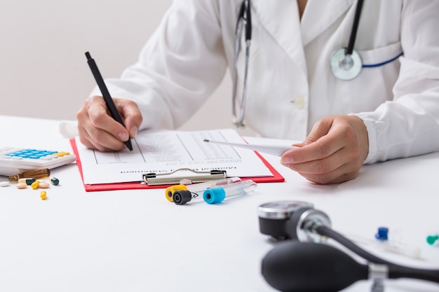 Doctor woman filling up prescription form while sitting at the desk in hospital close-up. Physician at work and ready to give an advice to help patient. 