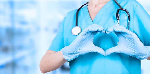 Doctor woman, hands in medical blue gloves, making a heart shape. We love you. Copy space. High quality photo