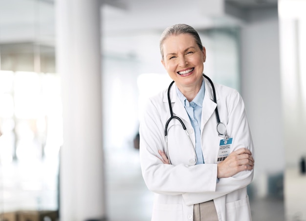 Женщина-врач и счастлива со скрещенными руками в больнице, стоит и улыбается за лекарство Зрелый человек и здравоохранение для исследовательского лечения или хирургии со специалистом по кардиологии со стетоскопом