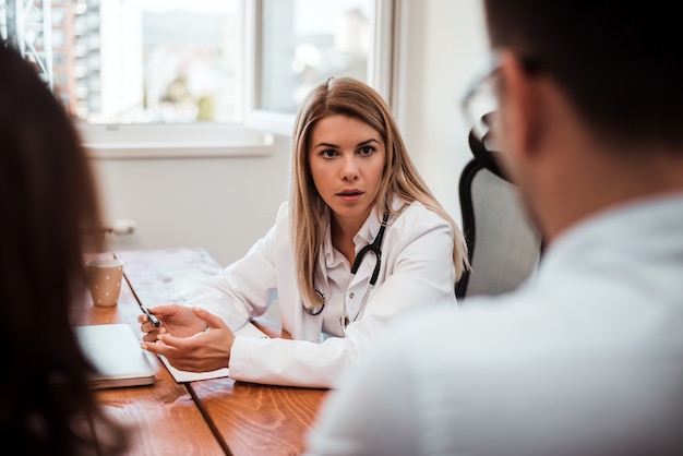 Doctor woman having conversation with young couple in office.