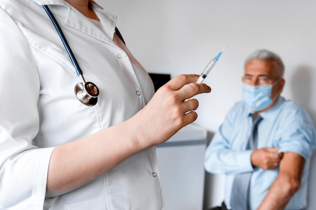 Doctor Woman Holding Syringe Before Make Injection to Old Patient in Medical Mask. Covid Vaccine. Doctor Giving a Senior Man Vaccination. Virus Protection. Fight against Covid-19, Coronavirus Concept.