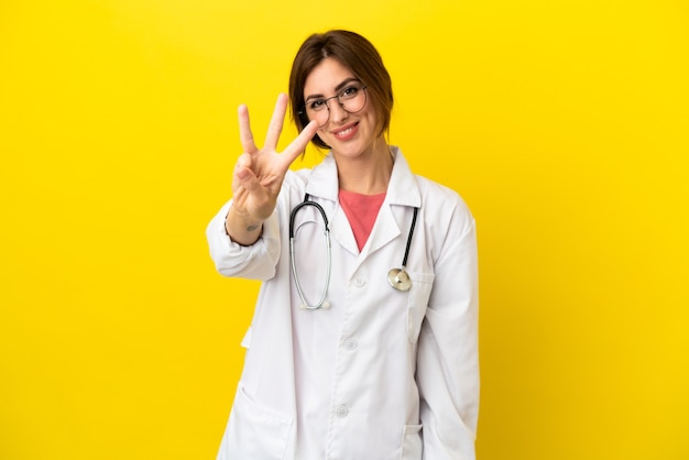 Doctor woman isolated on yellow background happy and counting three with fingers