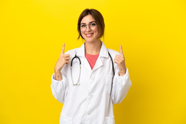 Doctor woman isolated on yellow background pointing up a great idea