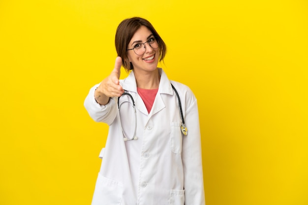 Donna medico isolata su sfondo giallo che stringe la mano per aver chiuso un buon affare