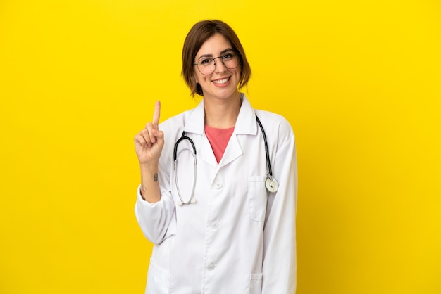 Donna medico isolata su sfondo giallo che mostra e alza un dito in segno del meglio