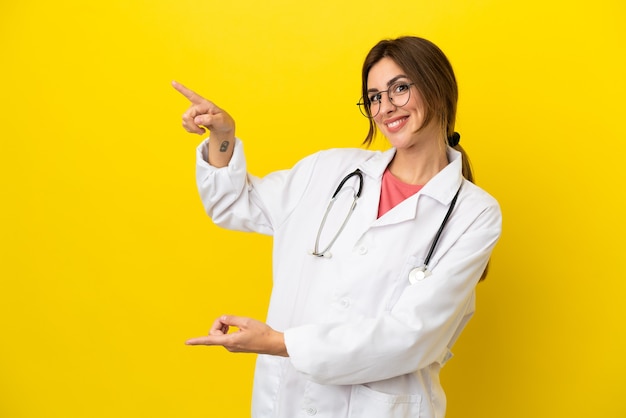 Doctor woman isolated on yellow surface pointing finger to the side and presenting a product