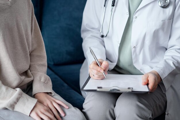 Doctor woman and kid boy patient at home medical exam. The pediatrician filling up medical form on clipboard, close up. Medicine, healthcare concepts