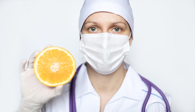 Doctor woman in medical protective mask with an orange closeup. Prevention and healthy eating during a pandemic.