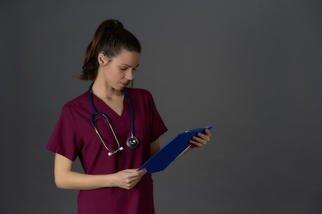 Donna medico in uniforme viola con stetoscopio guardando referto medico su sfondo grigio