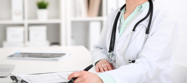 Doctor woman  sitting at the desk with computer at workplace in hospital office. Unknown physician's hands close-up. Green tone of blouse. Medicine and health care concept