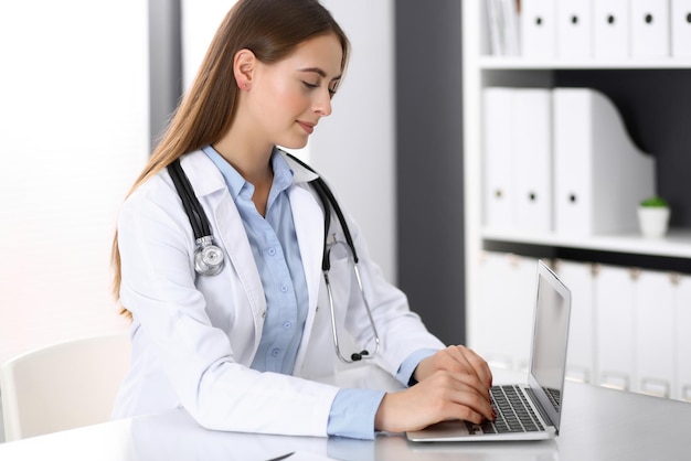 Donna del medico che digita sul computer portatile mentre si siede alla scrivania nell'ufficio dell'ospedale. medico al lavoro. concetto di medicina e assistenza sanitaria.