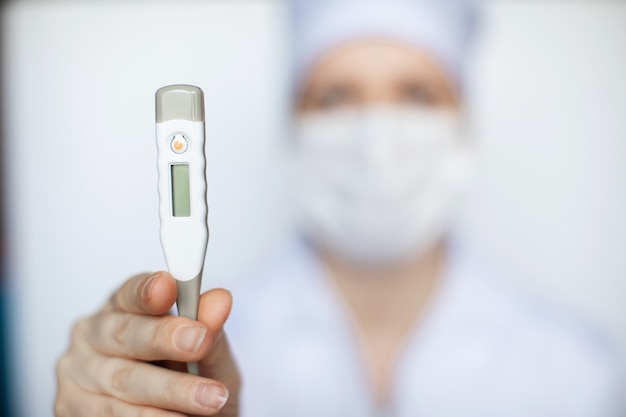 Doctor woman wearing medical face mask showing a medical thermometer