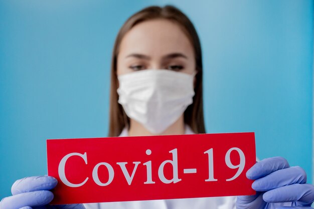 Foto aggiusti la donna con la maschera chirurgica che indica la carta rossa con il coronavirus del mesaage su fondo blu. organizzazione mondiale della sanità oms ha introdotto un nuovo nome ufficiale per la malattia di coronavirus chiamato covid-19