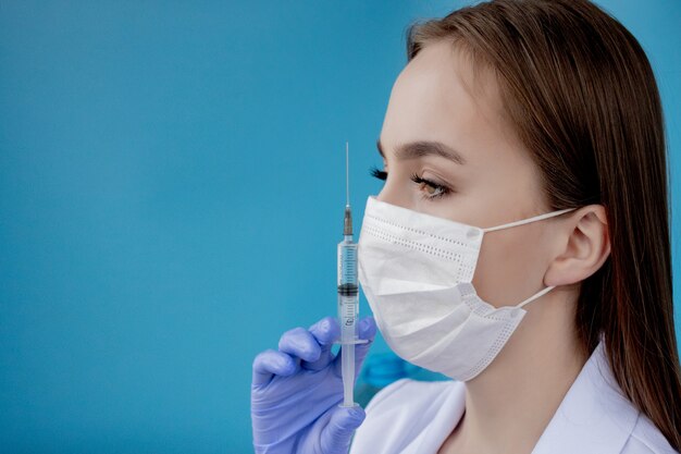 Doctor woman with surgical mask pointing to red paper with message Coronavirus on blue background. World Health Organization WHO introduced new official name for Coronavirus disease named COVID-19