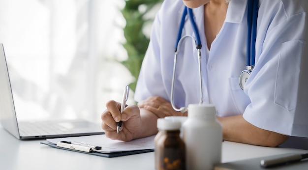 Doctor working on laptop computer writing prescription clipboard with record information paper folders on desk